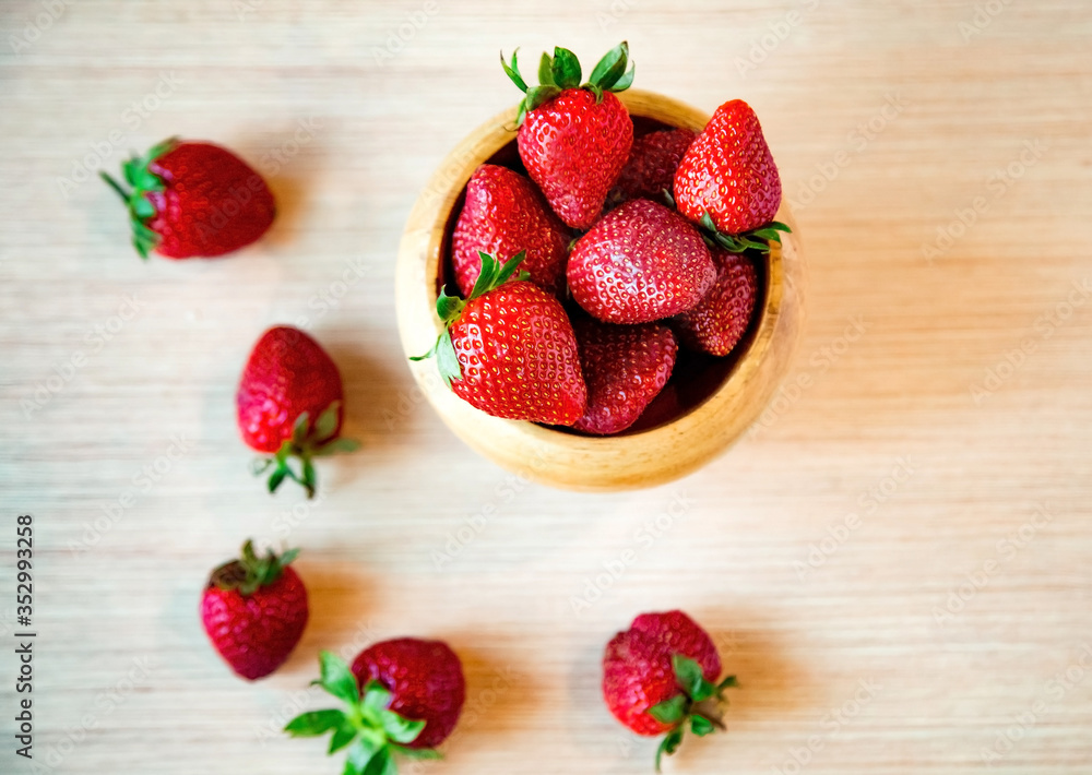 fresh strawberries, in a wooden plate, on a light wooden background