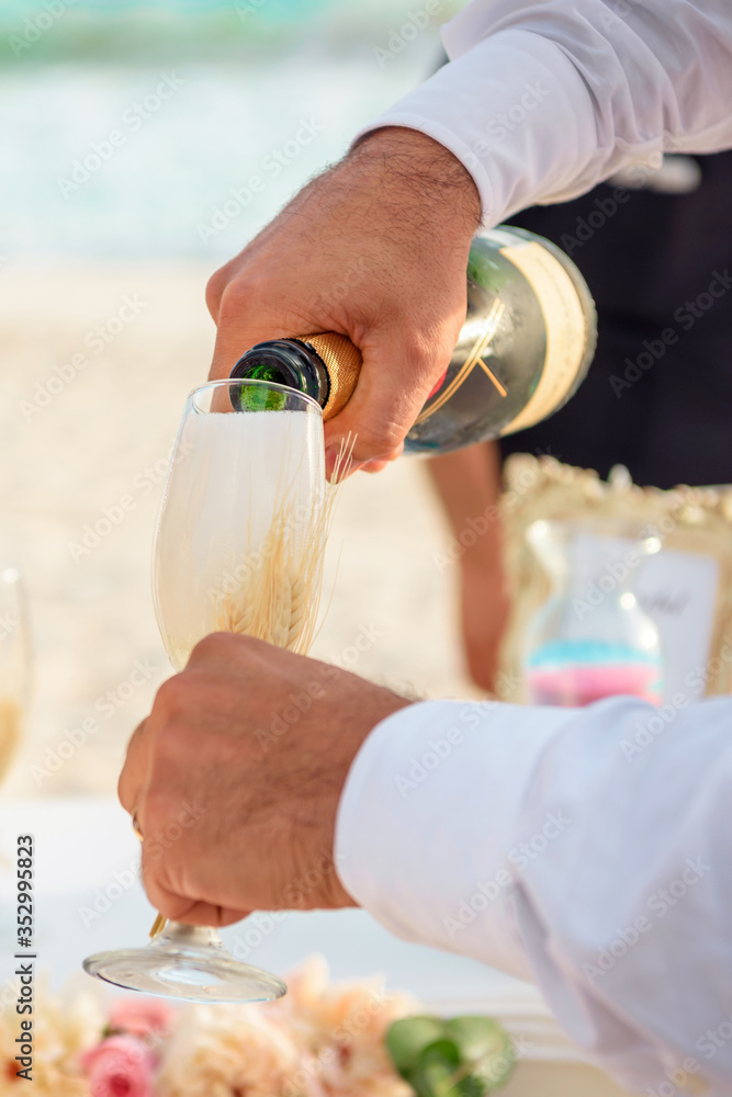 A man in a white shirt pours champagne into a glass, hands closeup.