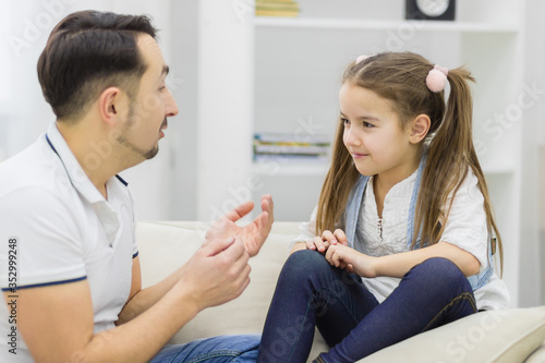 Father and daughter sitting on the sofa and having conversation.