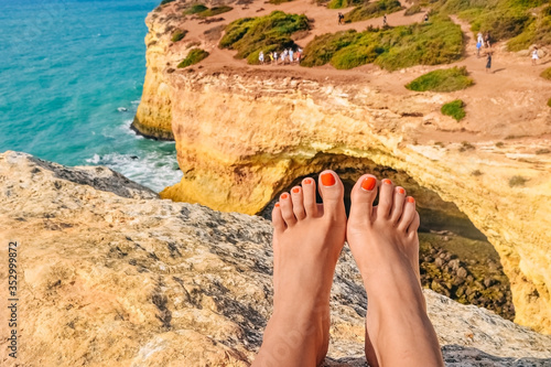 feet against a cliff on the famous Benagil beach in Portugal, waves crashing on the rocks, the raging ocean.