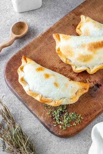 Traditional Argentine hot food made with meat and onion called empanada on wooden board and white background.
