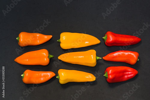Orange, red and yellow colored peppers lined up on a black surface