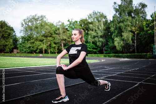 Healthy sports lifestyle. Athletic young woman in a sports dress doing fitness exercises. Fitness woman at the stadium. Young woman doing morning exercise. Young girl goes in for sports. Stretching. © Alex