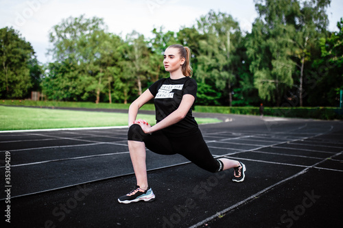 Healthy sports lifestyle. Athletic young woman in a sports dress doing fitness exercises. Fitness woman at the stadium. Young woman doing morning exercise. Young girl goes in for sports. Stretching.