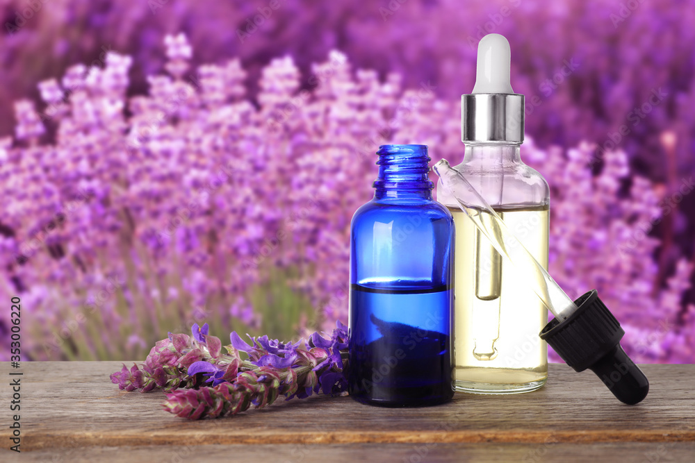 Bottles of essential oil and sage flowers on wooden table against blurred background. Space for text Bottles of essential oil and sage flowers on wooden table against blurred background. Space for text