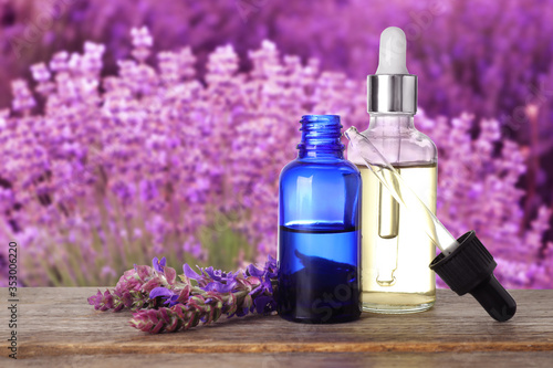 Bottles of essential oil and sage flowers on wooden table against blurred background. Space for text