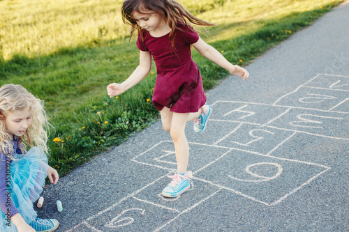 фотографія Cute adorable children girls friends playing jumping hopscotch outdoors