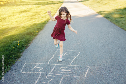 Cute adorable little young chld girl playing hopscotch outdoors. Funny activity game for kids on playground outside. Summer backyard street sport for children. Happy childhood lifestyle. photo