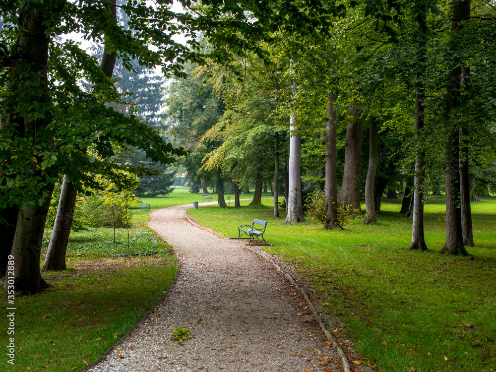 Curvy path winds through lush green grass and trees in the grounds surrounding Eggenberg Palace, Austria. 