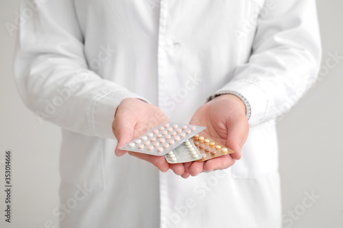Female gynecologist with birth control pills on grey background, closeup