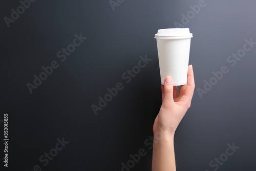 Fototapeta Naklejka Na Ścianę i Meble -  Hand with takeaway cup for drink on dark background