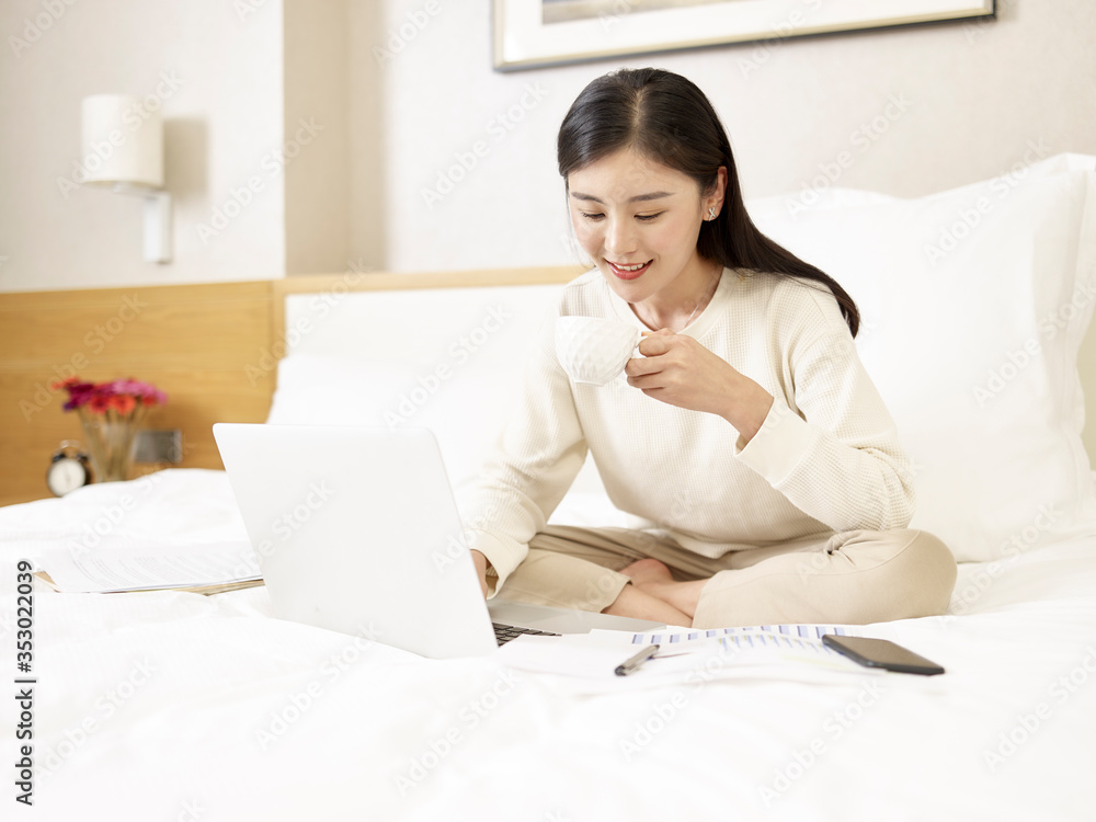 young asian business woman working from home holding a cup of coffee while using laptop computer young asian business woman working from home holding a cup of coffee while using laptop computer