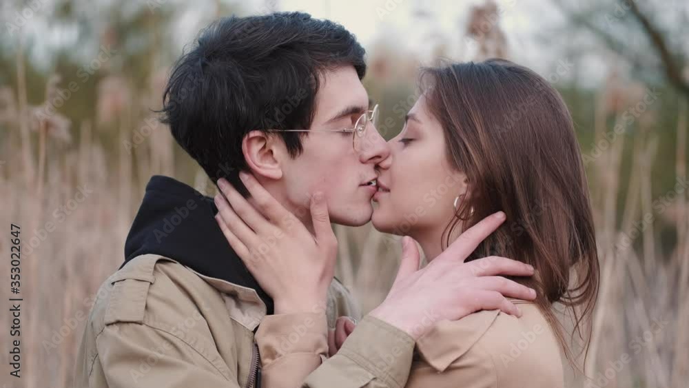 Couple is having date outdoors. Boy and girl are kissing in reeds. Brunette boy wears glasses. Couple is having date outdoors. Boy and girl are kissing in reeds. Brunette boy wears glasses.
