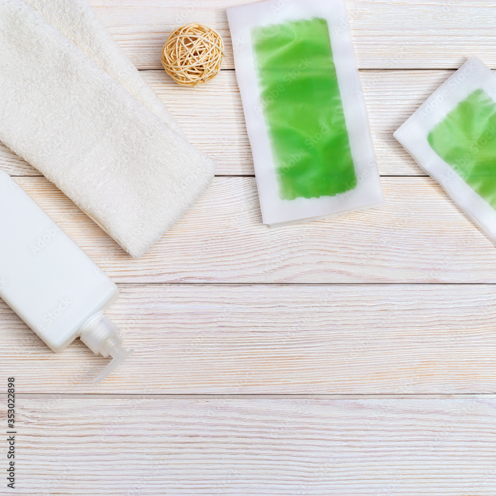 Set of female of hair removal. Wax strips, body moisturizer and white cotton towel on wooden background with copy space. Top view.