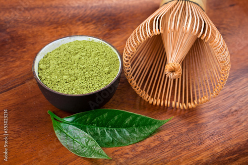 Fototapeta Naklejka Na Ścianę i Meble -  Powdered matcha tea in a cup and green leaves with bamboo matcha tea whisk also know as chasen on a wooden background.