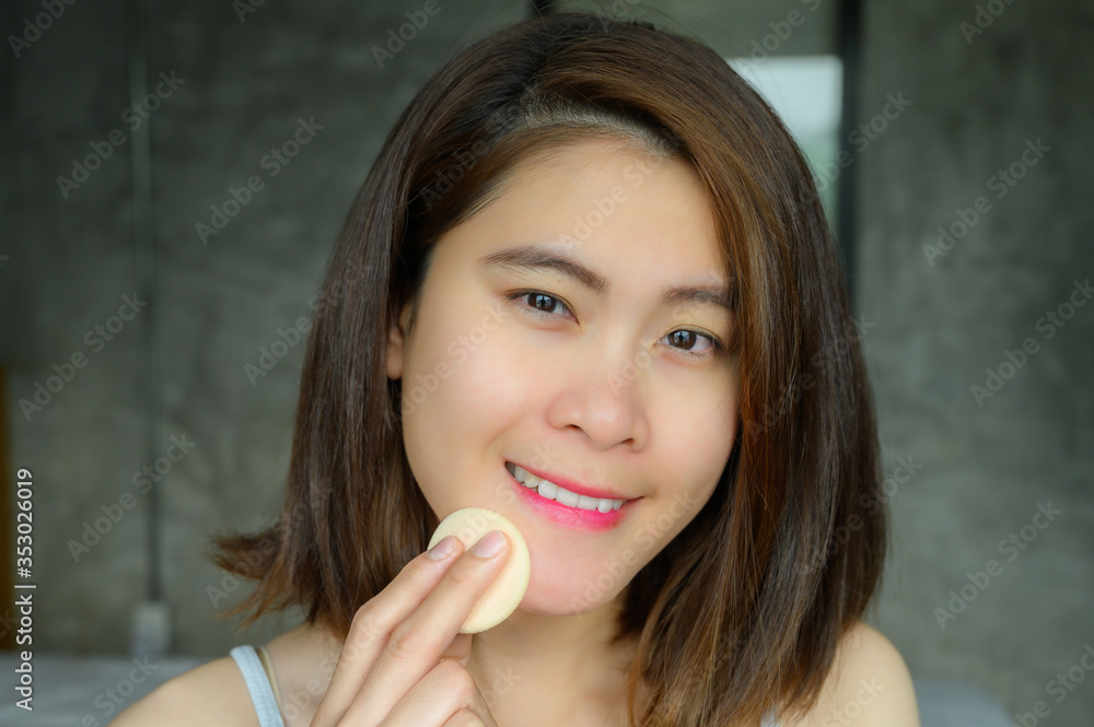 Portrait of young attractive Asian woman applying foundation powder puff on her face to cover flaws and change the natural skintone. Conceptual of women's beauty and cosmetic. Portrait of young attractive Asian woman applying foundation powder puff on her face to cover flaws and change the natural skintone. Conceptual of women's beauty and cosmetic.