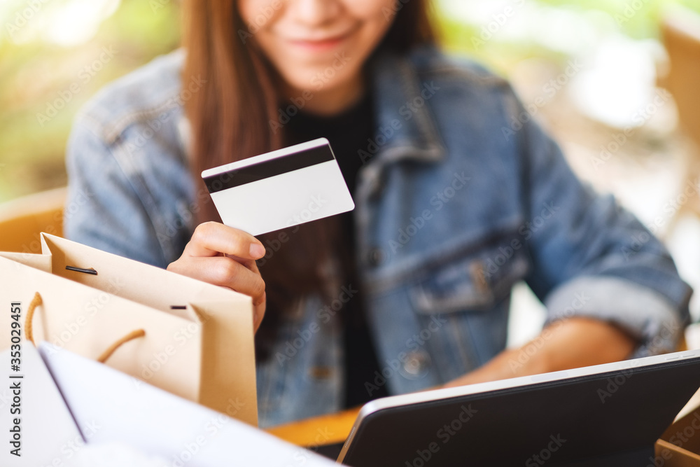 Obraz premium Closeup image of a young asian woman using tablet pc and credit card for online shopping with postal parcel box and shopping bags on the table