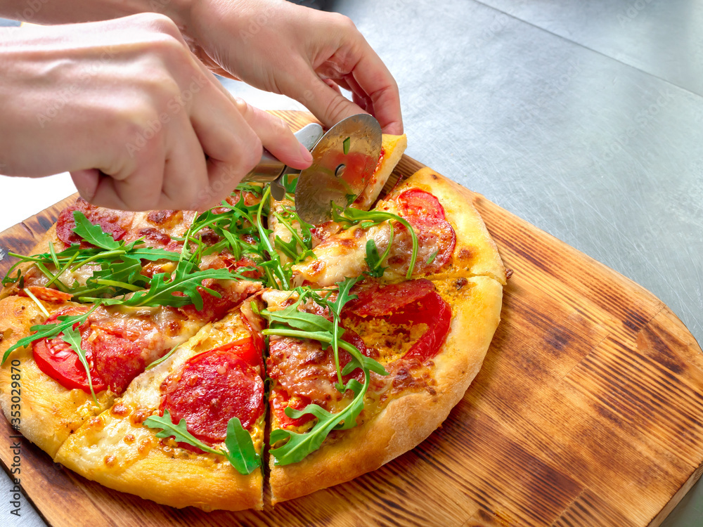 female hands cut pizza with a knife. Pizza with sausage, mozzarella and arugula. Pizza on a wooden board