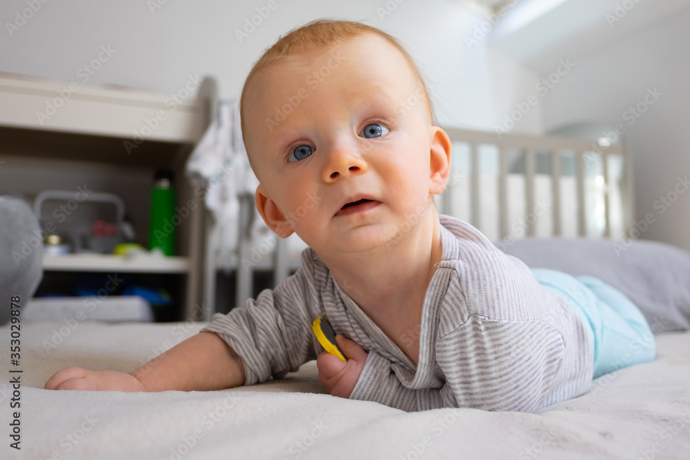 Concerned red-haired toddler holding yellow toy and looking aside. Cute baby girl with toy laying on bed in child room. Childhood and staying at home concept Concerned red-haired toddler holding yellow toy and looking aside. Cute baby girl with toy laying on bed in child room. Childhood and staying at home concept