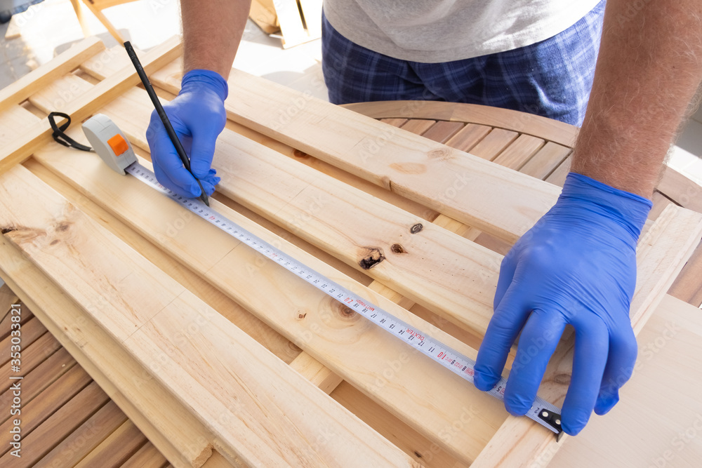 Craftsman assembling furniture, measuring wooden part with tape and pen. Closeup shot of male hands. Interior improvement concept Craftsman assembling furniture, measuring wooden part with tape and pen. Closeup shot of male hands. Interior improvement concept