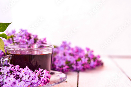 Cup of tea with lilac flowers on a wooden white background. Mocap for postcards. Spring time. Vase with lilacs. Copy space for text. The concept of holidays and good morning wishes