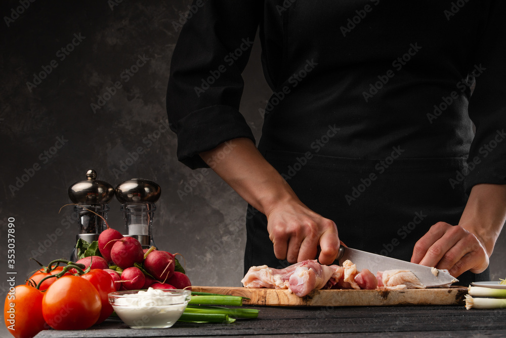 Chef cook prepares fresh chicken with vegetables. Against the background of a gray wall. Recipe book, home recipes. Cooking and gastronomy, restaurant business.