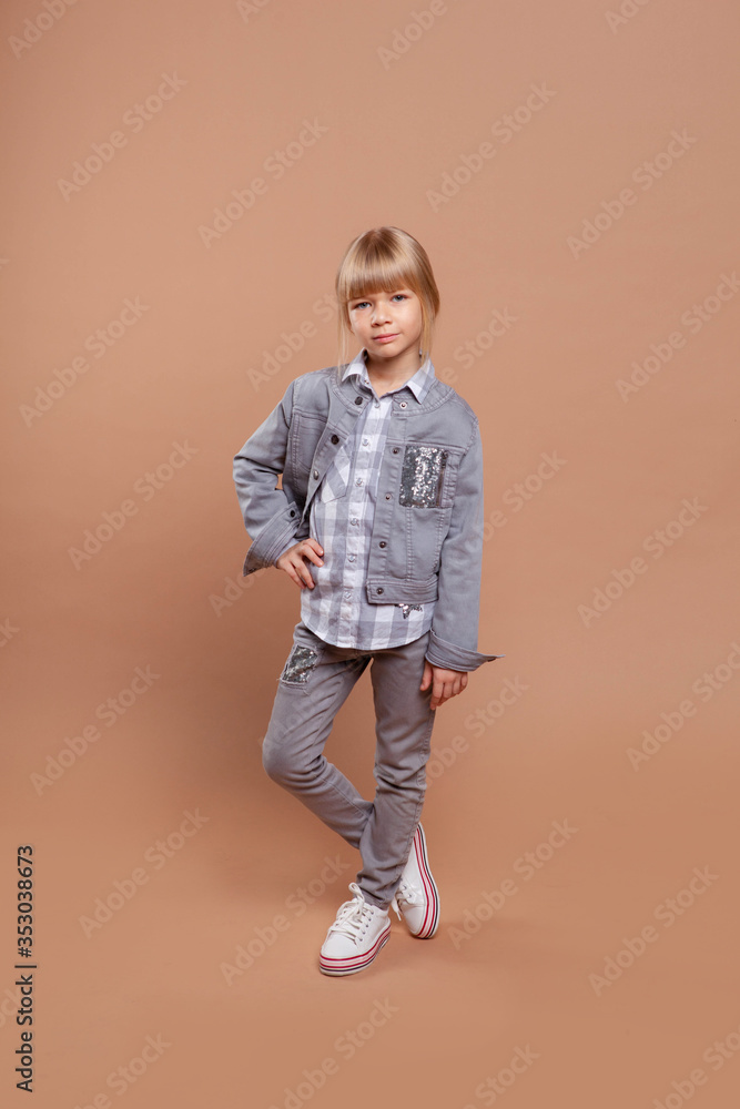 cute girl dressed in ordinary gray clothes stands on a beige background