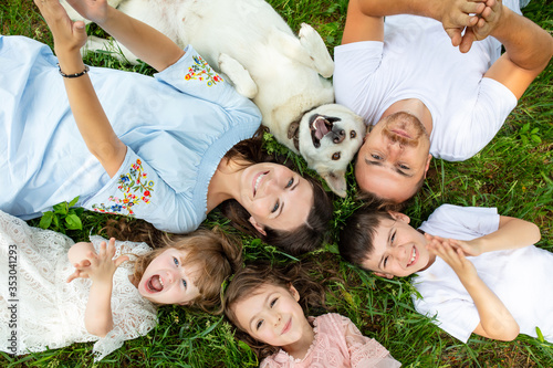 Happy beautiful big family together mother, father, children and dog lying on the grass top view