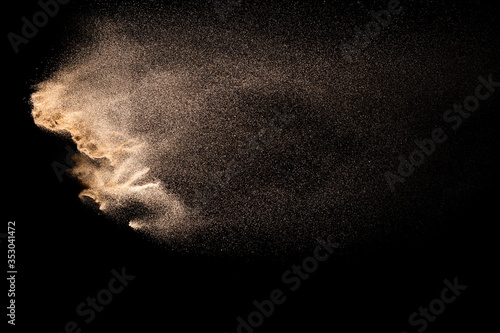 Golden sand explosion isolated on black background. Abstract sand cloud. Golden colored sand splash against dark background. Yellow sand fly wave in the air. photo