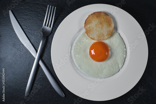 Breakfast of eggs on a white plate and black stone. Fork, knife on a black stone. Top view with copy space