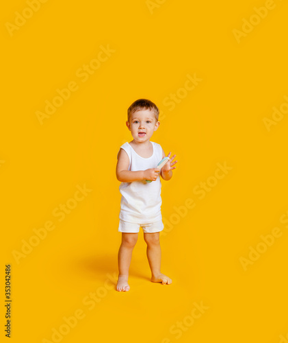 A little boy is standing in a white T-shirt and underpants and with a comb in his hands on an orange-yellow background