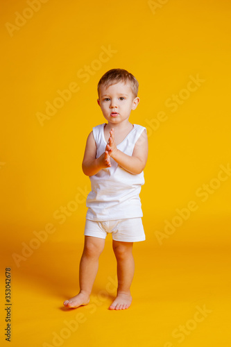Little boy stands in a white T-shirt and underpants on an orange-yellow background © Julie Boro