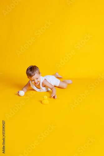little boy in a t-shirt and underpants on an orange-yellow background with a white Christmas ball in his hand