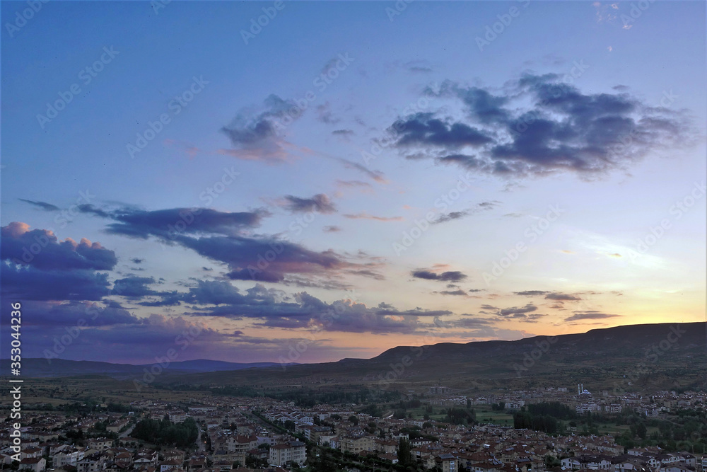 Beautiful sunrise in the valley of Cappadocia. In the distance, the sun rises from behind the mountain. The sky is colored by rays in golden, orange, pink tones. The clouds are blue and lilac.