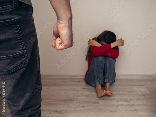 Male fist on the background of a frightened girl in a red shirt and jeans. Domestic violence.