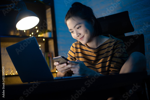 Asian woman happy take a break with smart phone and working on a laptop at the night at home. WFH. Work from home for avoid the Coronavirus COVID 19 concept.