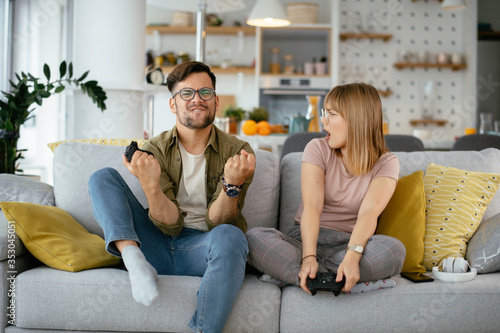 Husband and wife playing video game with joysticks in living room. Loving couple are playing video games at home. 