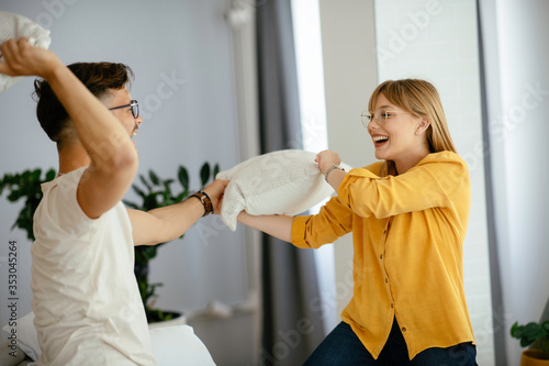 Young couple fighting pillows on the bed. Happy couple having fun at home.	 photo