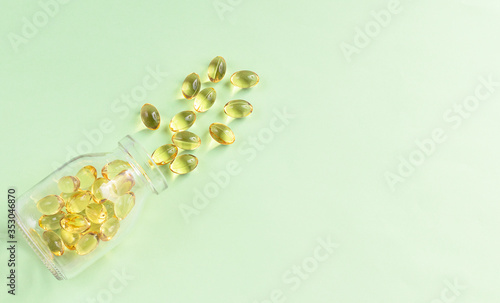 Yellow omega-3 capsules from a glass bottle on a green background. Copyspace for text. Health care, natural, natural supplements. Lifestyle concept