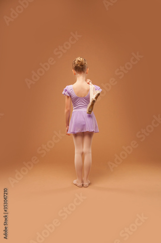girl in a ball gown and with pointe shoes on her shoulder stands back