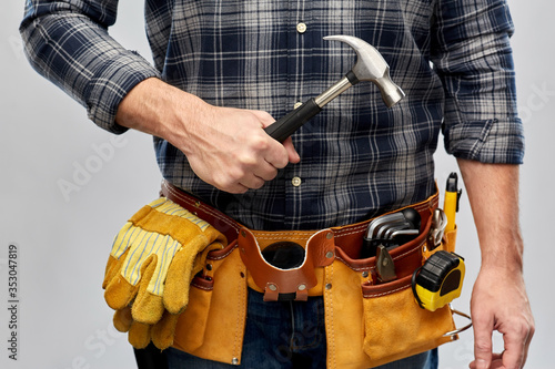 repair, construction and building - male worker or builder with hammer and working tools on belt over grey background