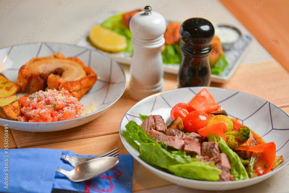 Salad with meat and vegetables. Italian cuisine, different dishes served in restaurant on light rustic wooden table.