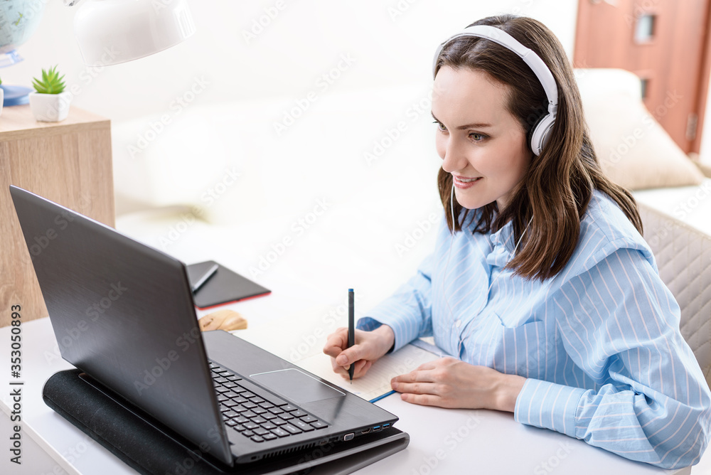 caucasian woman with headphones writes in notebook, looks at laptop screen, remote work at home, home training caucasian woman with headphones writes in notebook, looks at laptop screen, remote work at home, home training