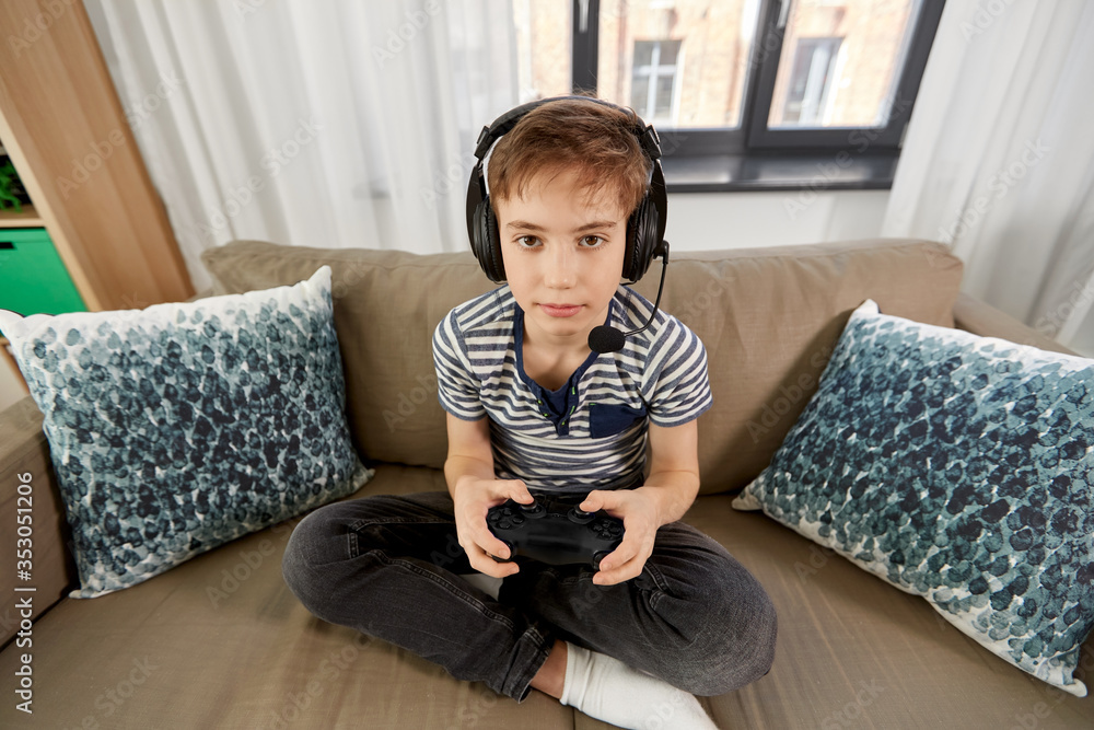 leisure, technology and children concept - smiling boy in headphones with microphone and gamepad playing video game at home