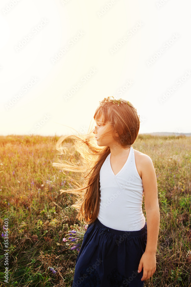 Pretty girl in wreath, with bouquet of wildflowers, with hair fluttering in wind stands at sunset on summer meadow. Copy space Pretty girl in wreath, with bouquet of wildflowers, with hair fluttering in wind stands at sunset on summer meadow. Copy space