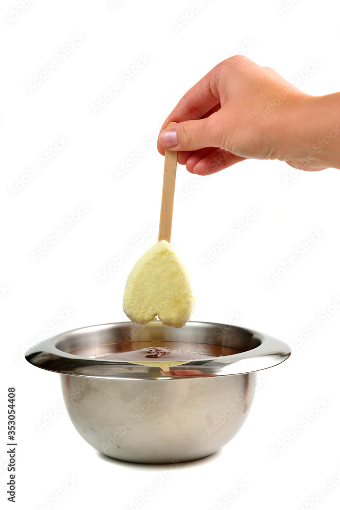 Hand dipping vanilla ice cream in heart shape on wooden stick in hot liquid dark chocolate Hand dipping vanilla ice cream in heart shape on wooden stick in hot liquid dark chocolate