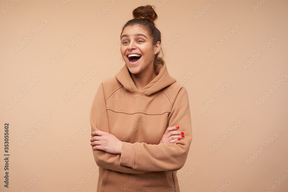 Indoor photo of young lovely brown haired lady with red manicure being in high spirit and laughing happily while standing over beige background with crossed arms Indoor photo of young lovely brown haired lady with red manicure being in high spirit and laughing happily while standing over beige background with crossed arms
