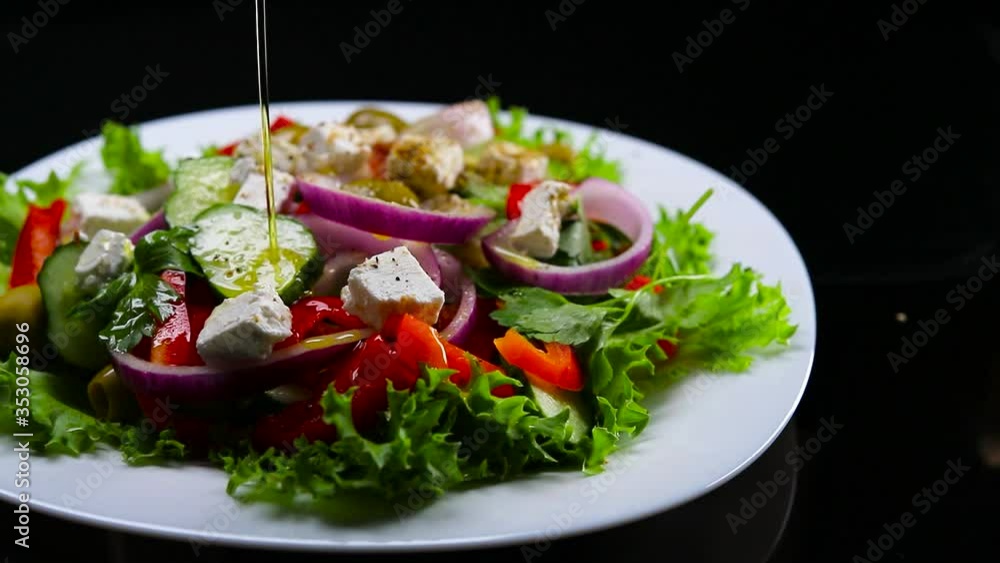 A black-gloved cook pours olive oil over a Greek salad A black-gloved cook pours olive oil over a Greek salad
