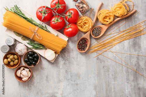Different uncooked pasta, vegetables and spices on grey background