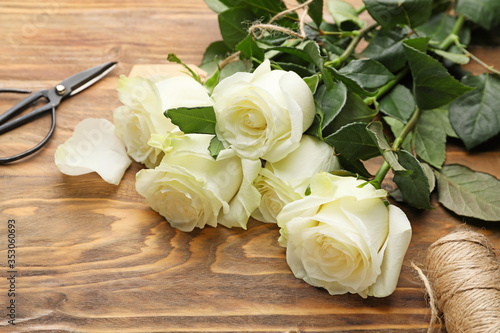 Beautiful white roses, thread and scissors on wooden background © Pixel-Shot